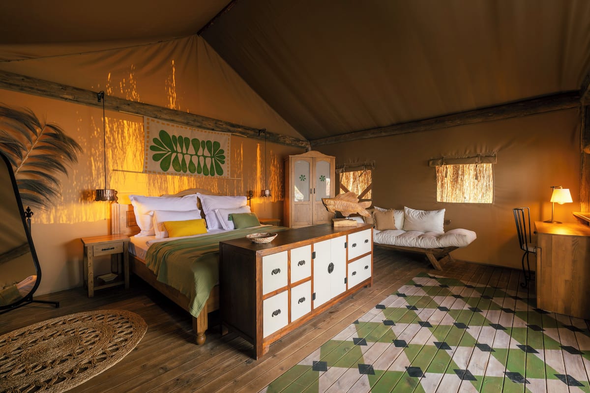 A tented accommodation with a bed, a wooden cabinet, a sofa, and a dining area.