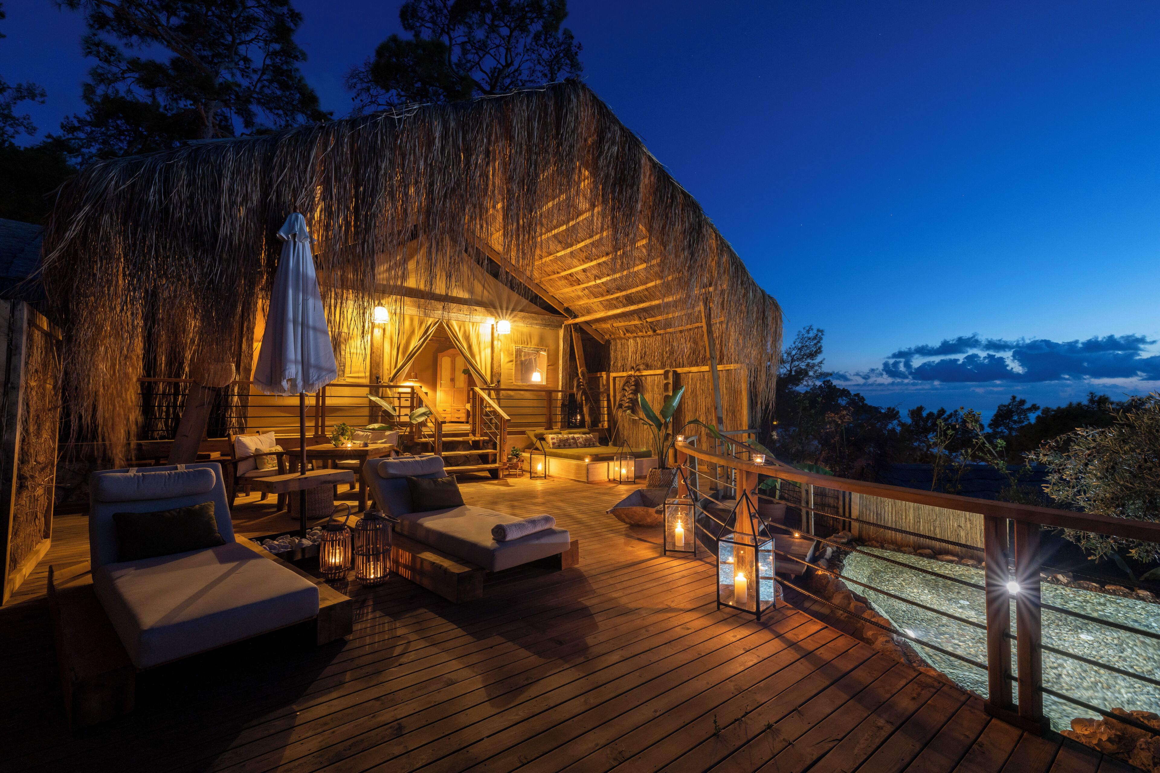 A wooden deck with lounge chairs and a staircase leading to a thatched-roof building.