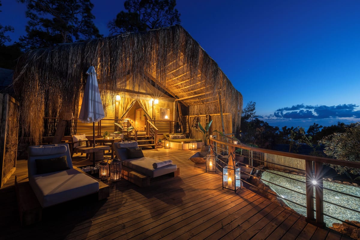 A wooden deck with lounge chairs and a staircase leading to a thatched-roof building.