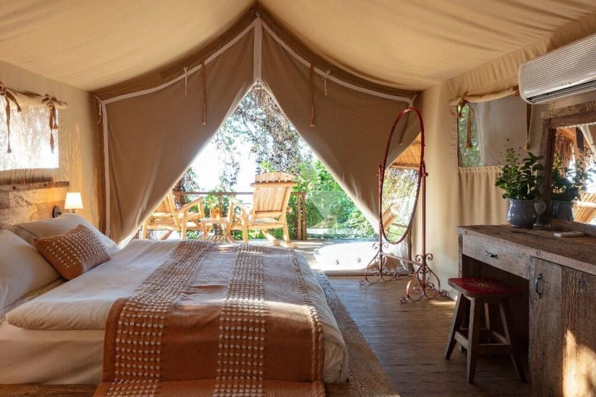 A tented room with a bed, a desk, and a chair. There is a window and a view of the outdoors.