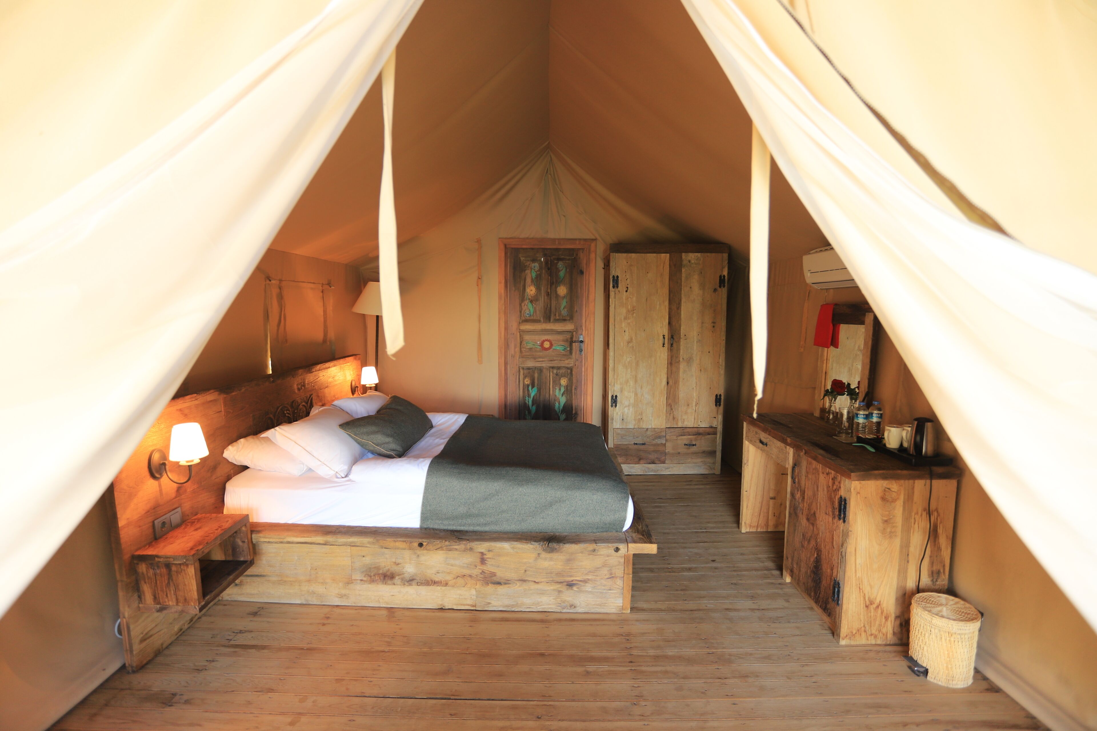 A tent-style bedroom with a bed, bedside table, lamp, and wardrobe.
