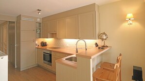 Una cocina compacta con horno integrado, un lavamanos y un pequeño comedor con una silla.