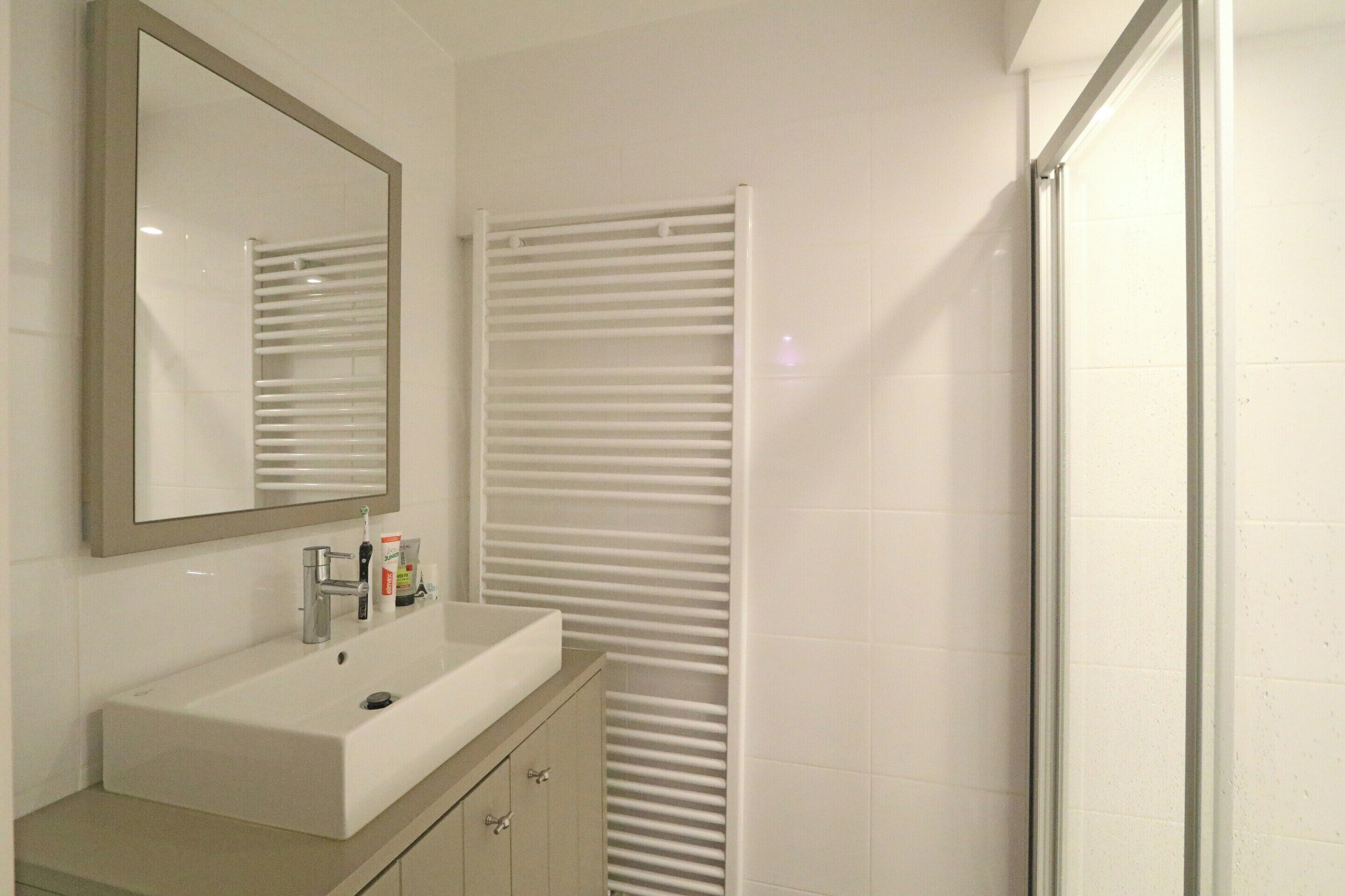 Un baño con lavamanos blanco, espejo y toallero.