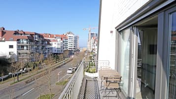 Un balcón con vistas a una calle de la ciudad, una grúa de construcción y edificios modernos.