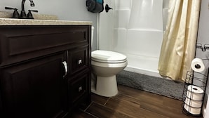 Un baño con tocador de madera oscura, inodoro blanco y ducha con cortina color beige.