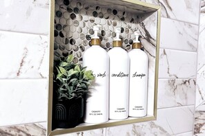 A bathroom shelf with three white bottles labeled 'wash conditioner shampoo' and a potted plant. - Tulum Stay at Austin by The Key Rentals (Austin)