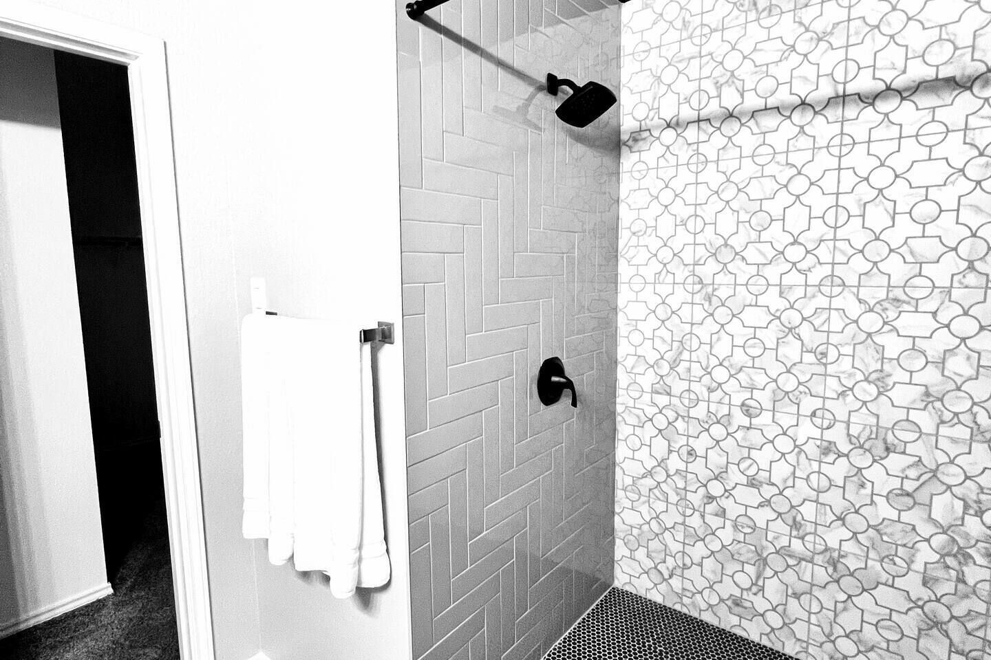 Un bagno con un motivo a spina di pesce nella piastrellatura, una doccia con soffione nero manuale e una parete rivestita di piastrelle decorate.