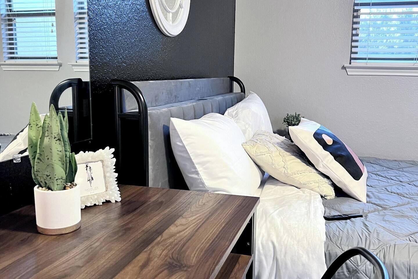 Habitación de hotel con cama, mesita de noche con planta en maceta, un detalle decorativo y ventana con persianas.
