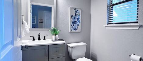 A bathroom with a white toilet, a sink with black faucets, a mirror above the sink, and a framed floral artwork on the wall.