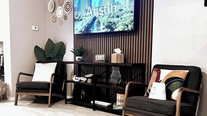 Un salon avec deux fauteuils, un téléviseur fixé au mur, des assiettes décoratives et une plante en pot.
