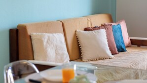 A room with a beige sofa, two pillows, a glass table with breakfast items, and framed pictures on the wall.