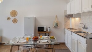 A modern kitchen with white cabinets, a glass dining table, and a microwave.