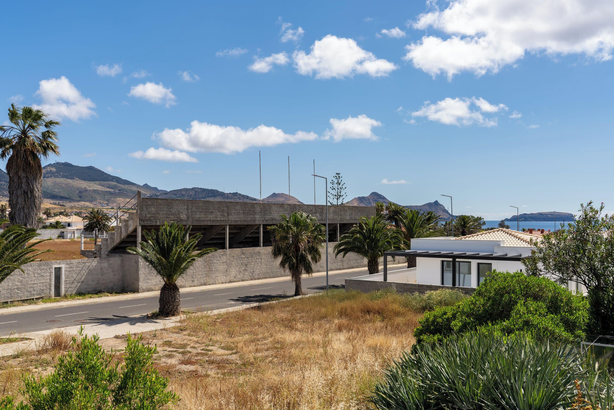 Un edificio moderno con fachada de concreto, una carretera en primer plano y palmeras.