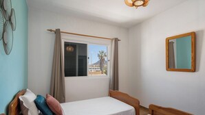 A bedroom with two single beds, a window with curtains, a mirror on the wall, and a ceiling fan.