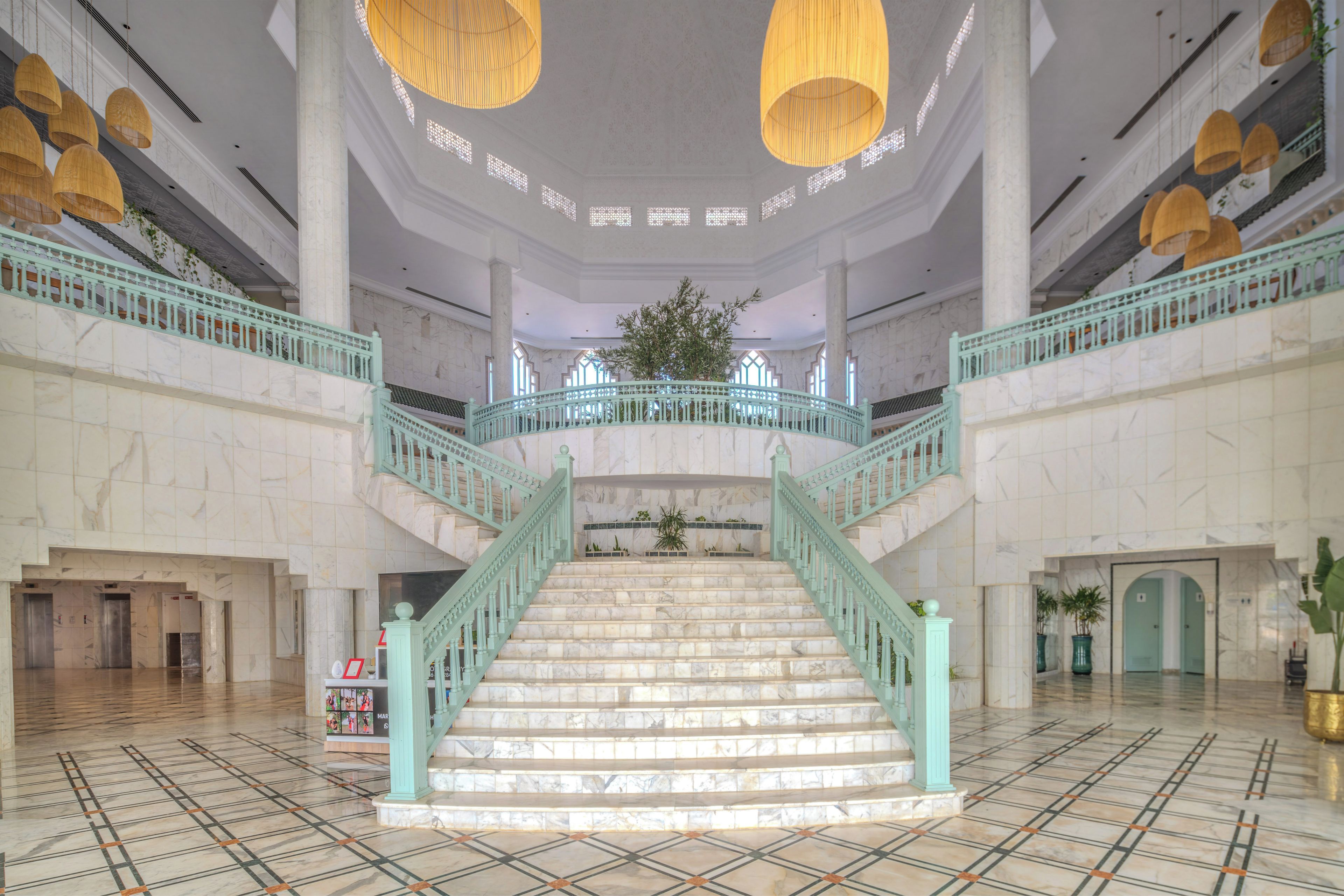 Una gran escalera con escalones de mármol y barandales color turquesa que conduce a un balcón en el segundo piso.
