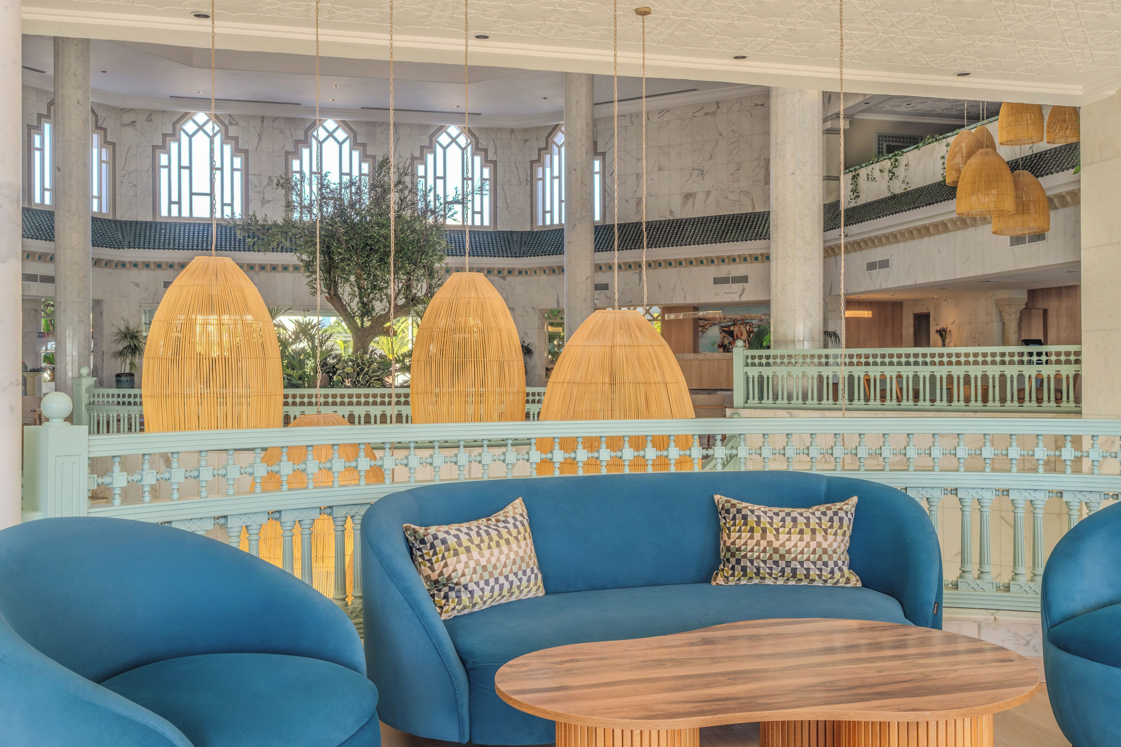 A spacious lobby with a blue sofa set, hanging rattan lamps, and a view of a traditional building with tiled roofs.