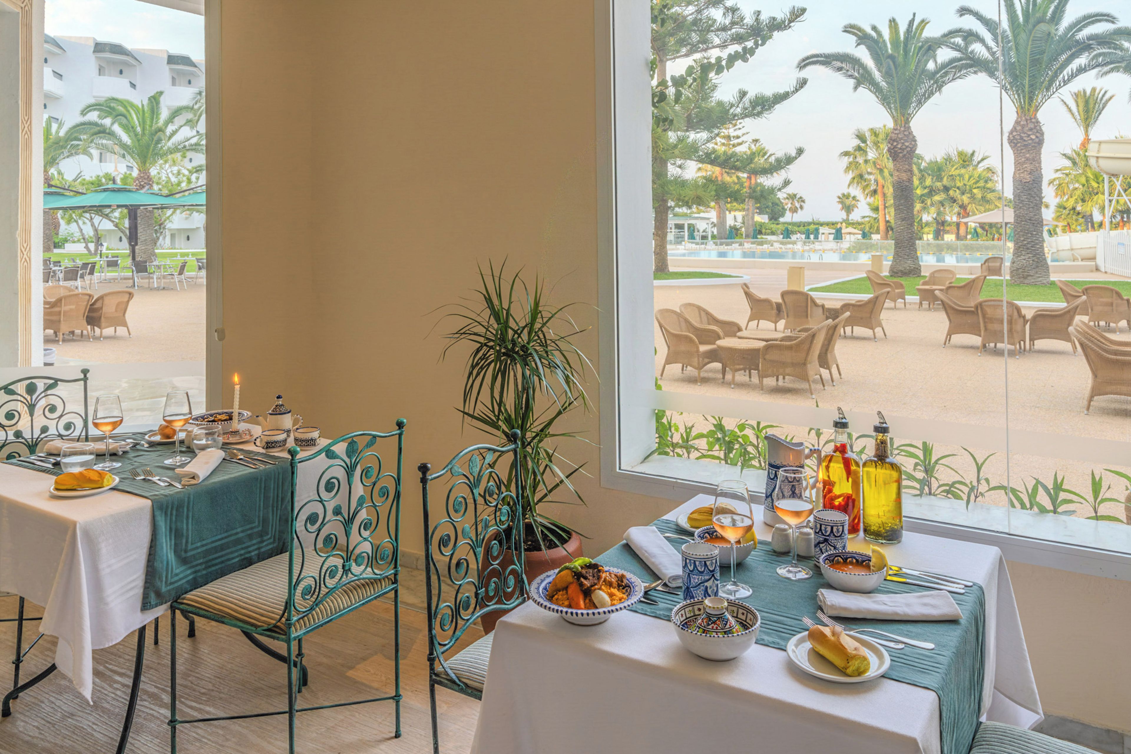 A dining area with a table set for two, a potted plant, and a view of the outdoor seating area.