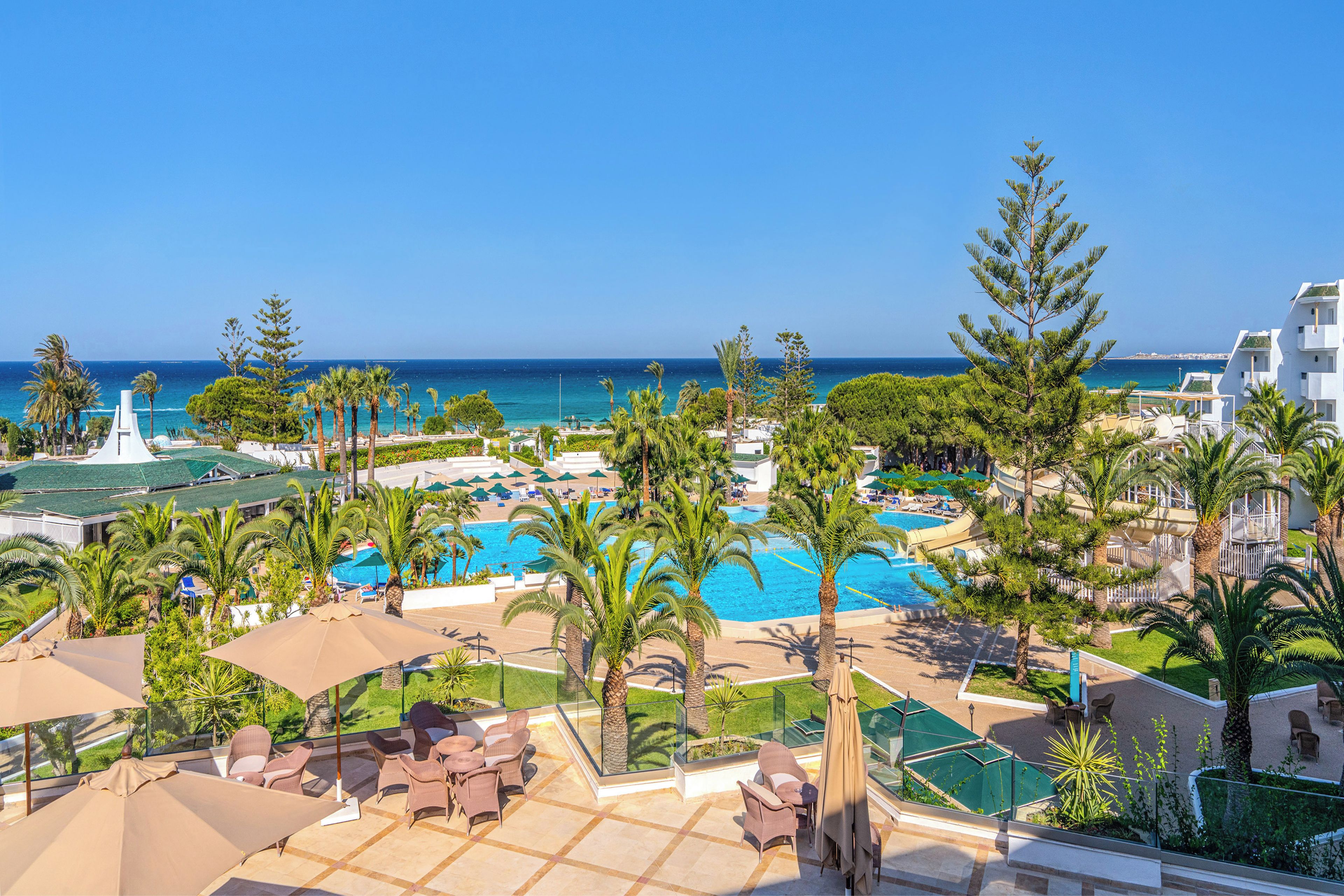 Ein Resort mit mehreren Schwimmbecken, Palmen und Blick auf das Meer.