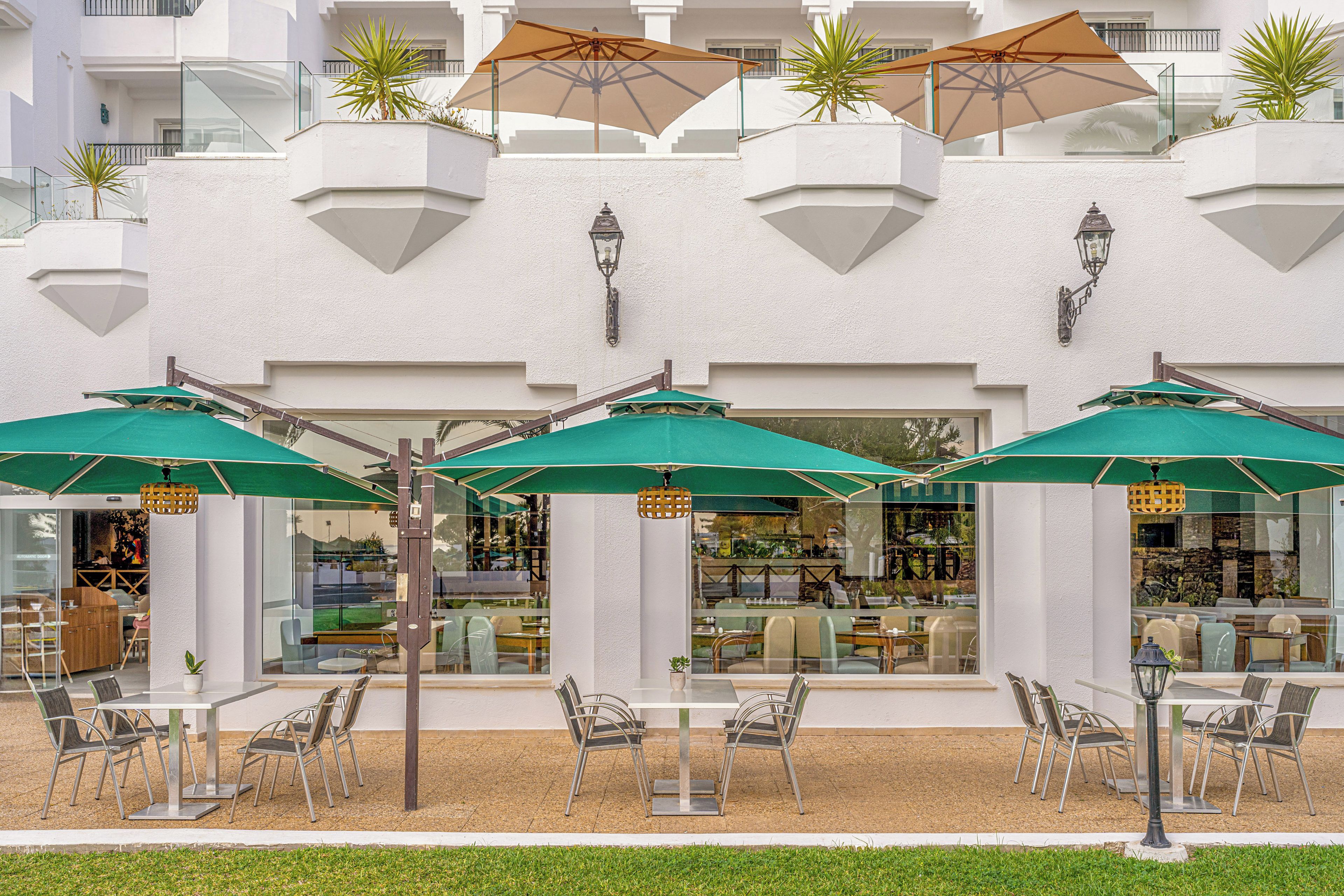 A hotel with outdoor seating, umbrellas, and a white facade.