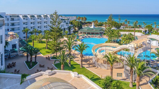 Un resort con una piscina grande, palmeras y vista al océano.