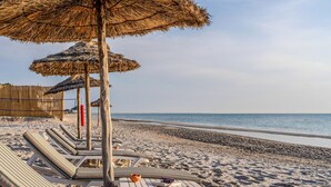 Una playa con sillas de descanso y sombrillas de paja.