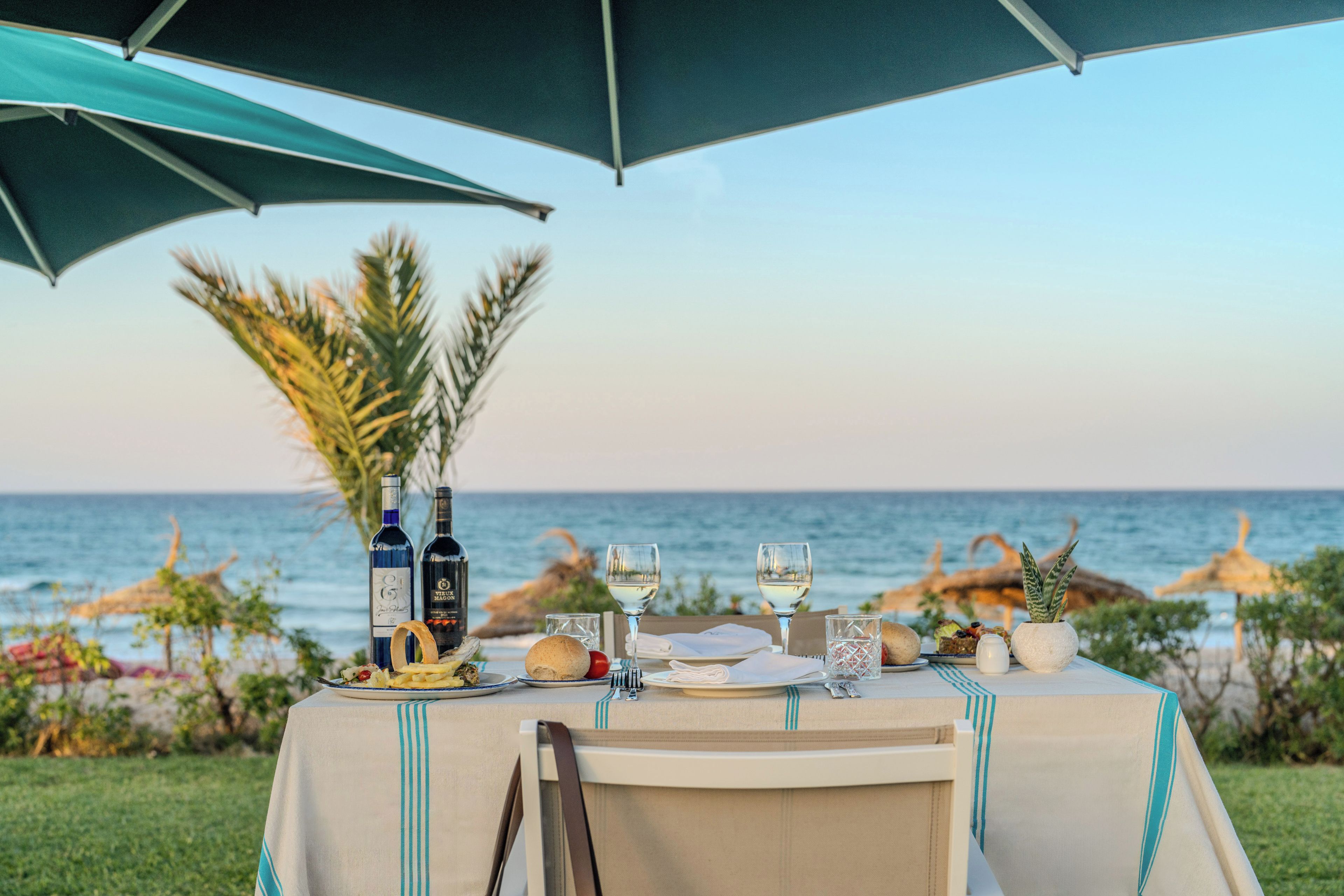 An outdoor dining table with a view of the sea, a bottle of wine, and a glass of water.