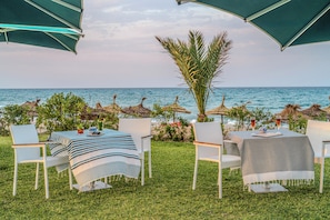 Un espace extérieur aménagé pour les repas, avec des tables et des chaises, un palmier et une vue sur la mer.