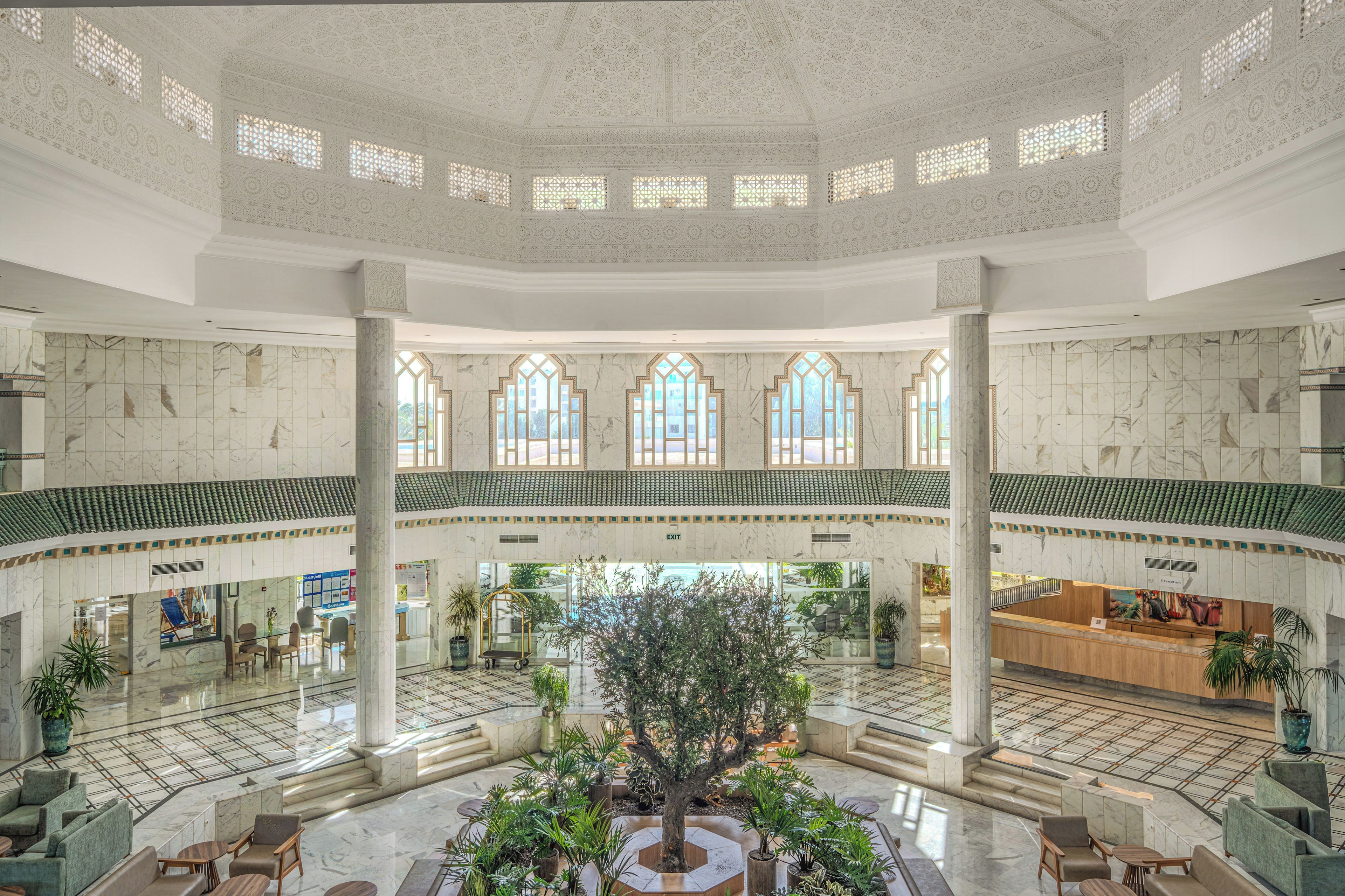 A spacious lobby with a central atrium, marble flooring, and a reception desk.