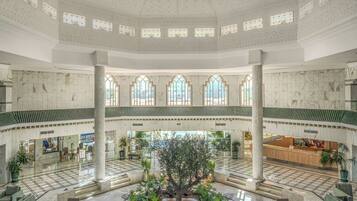 A spacious lobby with a central atrium, marble flooring, and a reception desk.