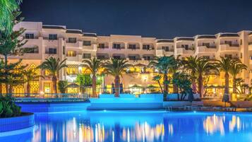 Ein Hotel mit Schwimmbad, Palmen und nächtlicher Beleuchtung.