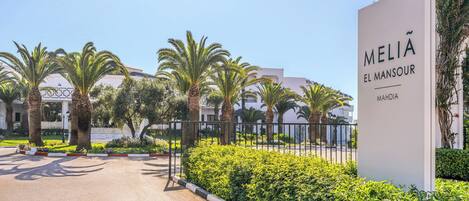 A gated entrance to a property named 'MELIA EL MANSOUR' with a clear sky and palm trees.