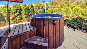 A hot tub with wooden steps and a metal railing, surrounded by a wooden deck and a view of a forested area. - Amazing apartment in Szyldak with sauna (Szyldak)
