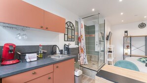 A compact kitchen with a coffee machine, sink, and a glass shower enclosure.