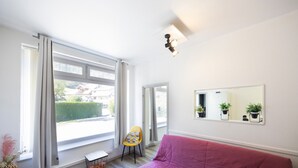 A room with a large window, a red sofa, a chair, a small table, and a mirror with potted plants. - 10 mins from annecy, apartment apartment near the lake (Sevrier)