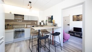 A modern kitchen with a central island, bar stools, a built-in oven, and a dining area with a pink chair. - 10 mins from annecy, apartment apartment near the lake (Sevrier)