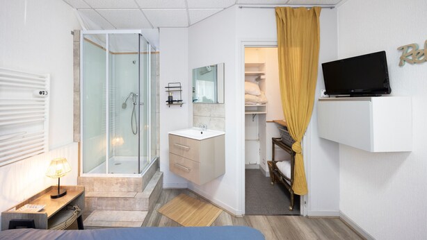 A modern hotel room with a shower, sink, mirror, TV, and a bed. - 10 mins from annecy, apartment apartment near the lake (Sevrier)