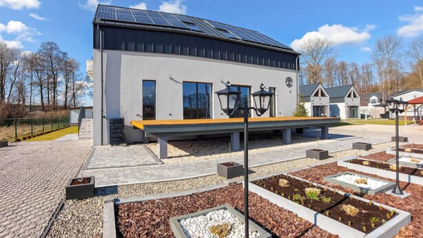 A modern building with a solar panel roof, a bench, and a garden area with raised beds.