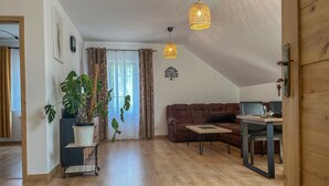 A spacious living area with a wooden floor, a brown sofa, a dining table, and a potted plant.