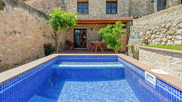 Un edificio de piedra con piscina, mobiliario exterior y un porche cubierto.