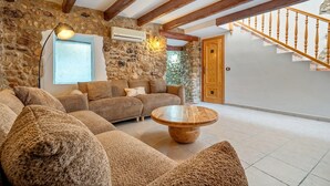 Una sala de estar con pared de piedra, vigas de madera, un sofá, una mesa de centro y una escalera.