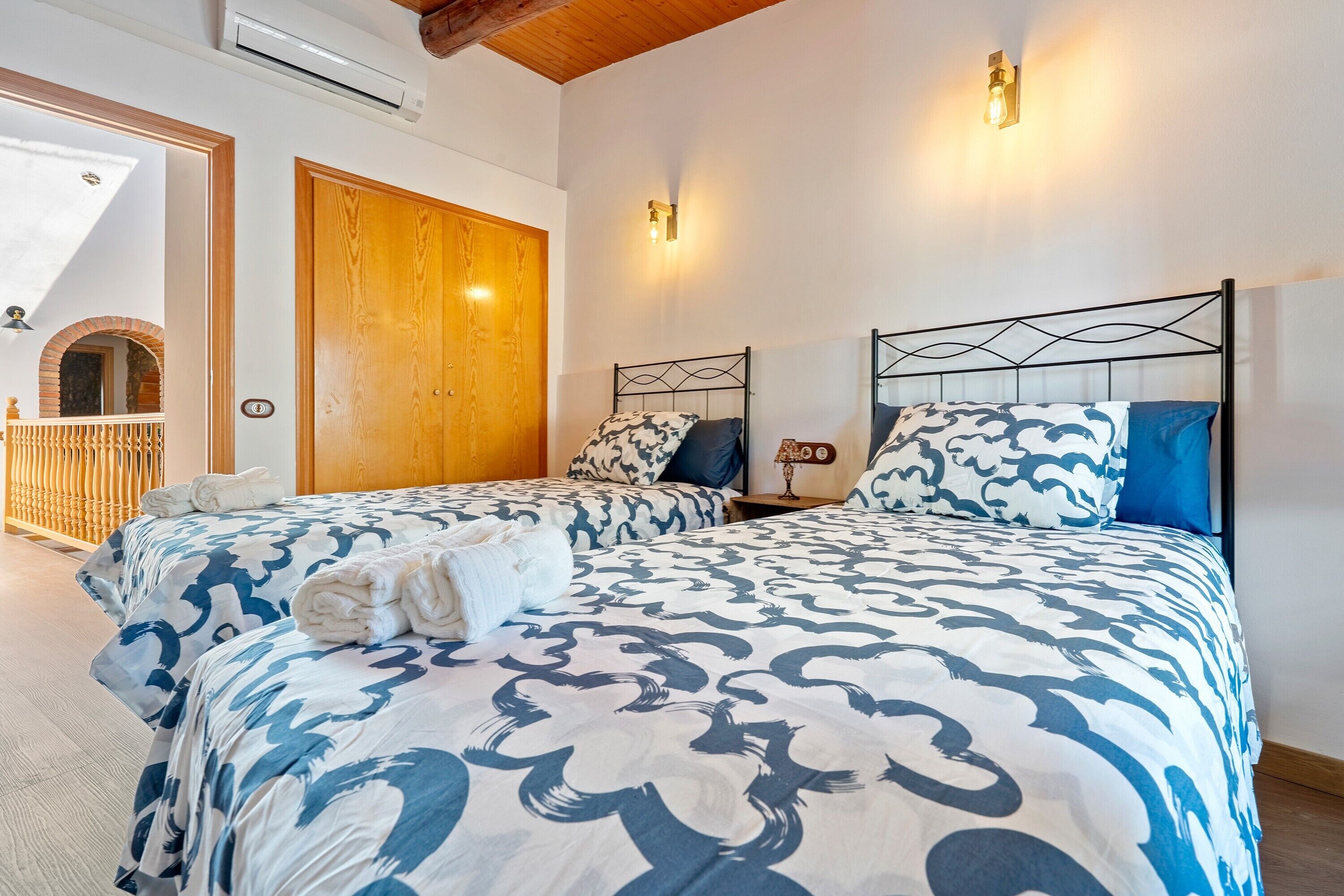 Un dormitorio con dos camas, una puerta de madera, un balcón y una lámpara fijada a la pared.