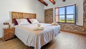 Un dormitorio con cabecera de madera, un ventanal con vistas, una mesita de noche y una cama con colcha estampada.