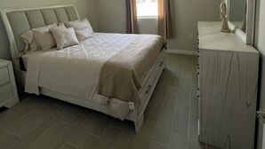 A bedroom with a bed, a dresser, a mirror, and a window with curtains.
