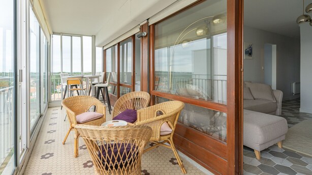 Un balcon avec des fauteuils en osier, une table et un canapé.
