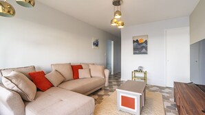 Un salon comprenant un canapé, une table basse, un meuble pour la télévision, un luminaire suspendu et une porte.