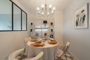 A dining area with a round table, chairs, a chandelier, and a framed artwork on the wall. - Apartment 'La Résidence' with Sea View, Private Terrace and Wi-Fi (Saint-Georges-de-Didonne)