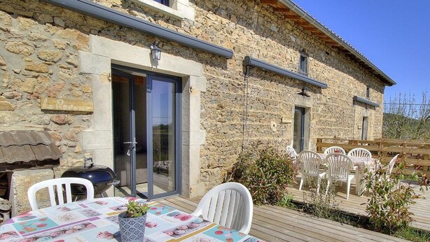 A stone building with a patio area featuring a table with a colorful tablecloth, white chairs, and a small potted plant. - Les Gîtes de Bellevue, Le Rêveur (THURINS)
