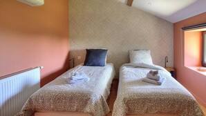 Two single beds with patterned bedding, a radiator, and a window with a view. - Les Gîtes de Bellevue, Le Rêveur (THURINS)