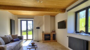 A modern living room with a wooden ceiling, a fireplace, a sofa, a TV, and a large window. - Les Gîtes de Bellevue, Le Rêveur (THURINS)