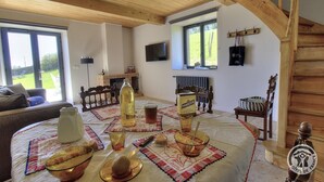 A cozy living room with a wooden ceiling, a fireplace, a dining table set with a bottle, glasses, and a bowl. - Les Gîtes de Bellevue, Le Rêveur (THURINS)